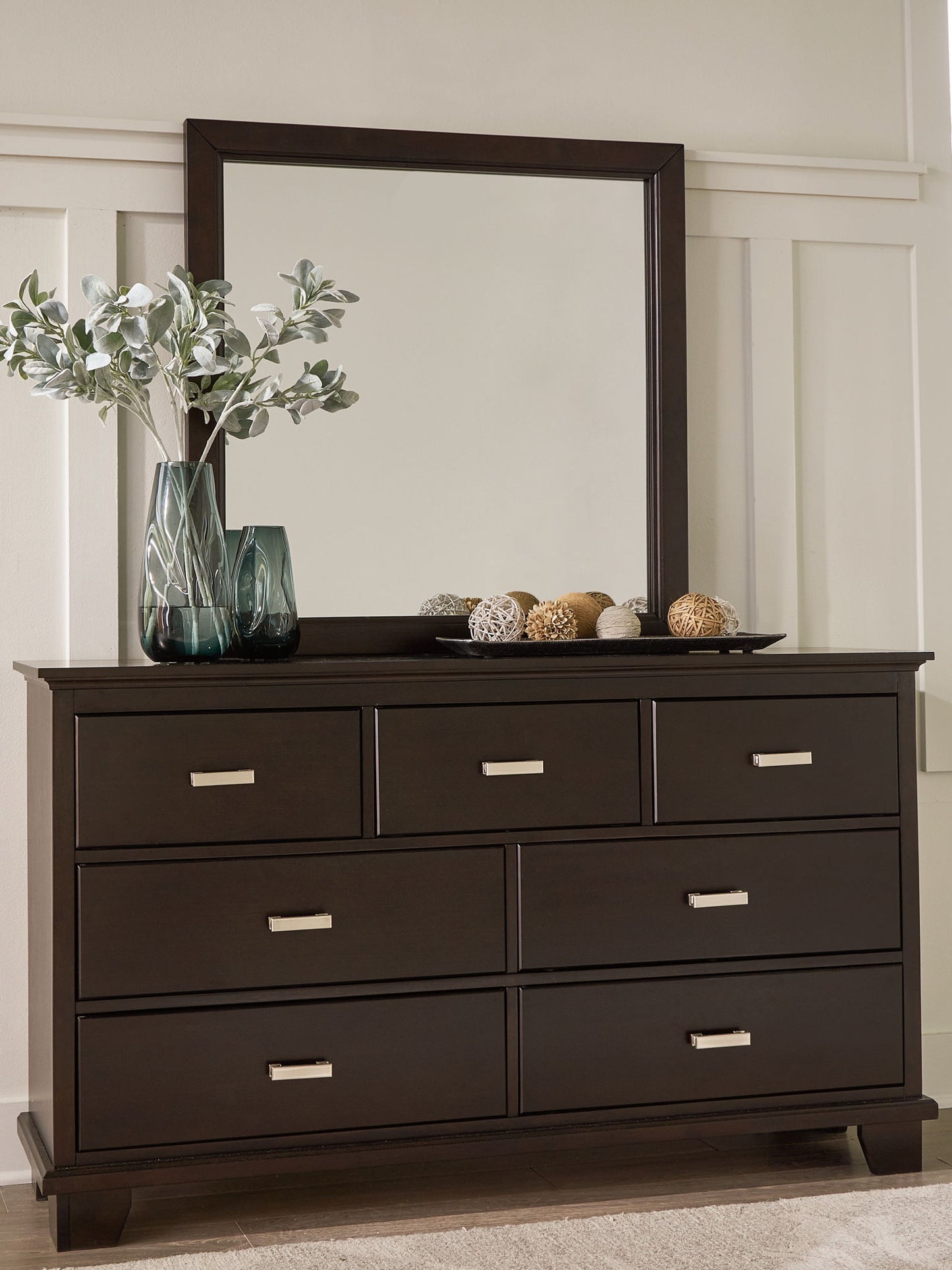 Dark wood dresser with a mirror, potted greenery, and decorative bowl on top.